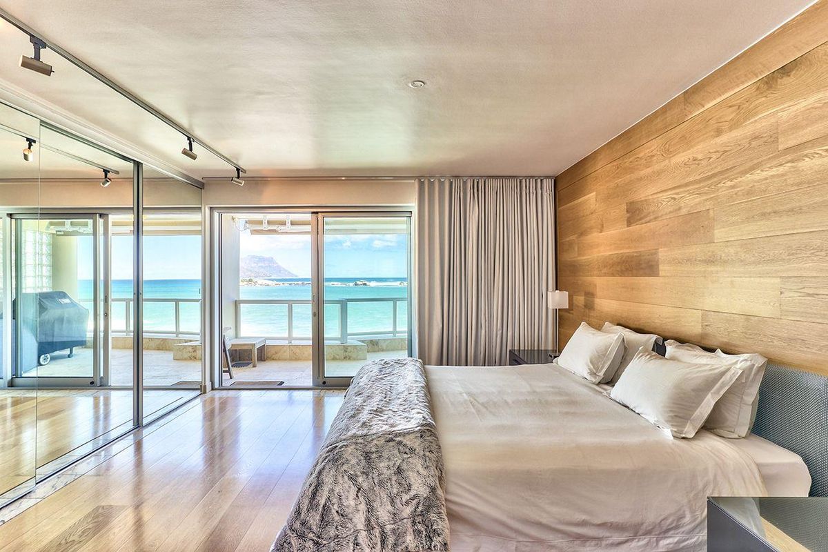 Spacious bedroom featuring hardwood flooring, a wood panel feature wall, mirrored wardrobes, and sliding glass doors opening to a balcony with ocean views.