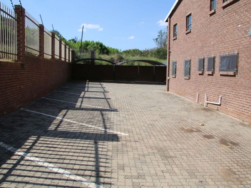 A paved rear parking area featuring brick boundary walls with electric fencing and security grilles on the building windows.