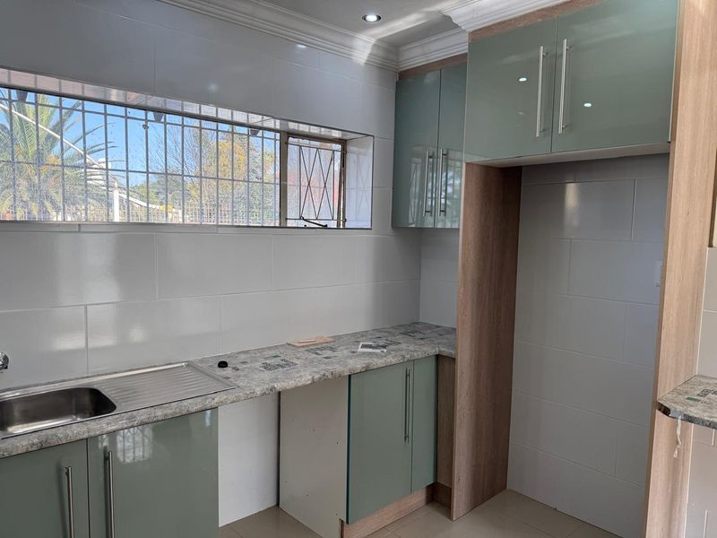 Modern kitchen featuring sleek two-tone cabinetry, stone-look laminate countertops, stainless steel sink, and tiled splashbacks in a clean, well-lit space.