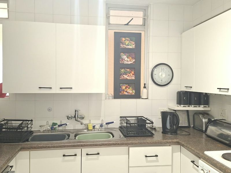 A functional kitchen featuring white cabinetry, a double basin sink, tiled backsplash, and integrated appliances including a microwave and electric hob.