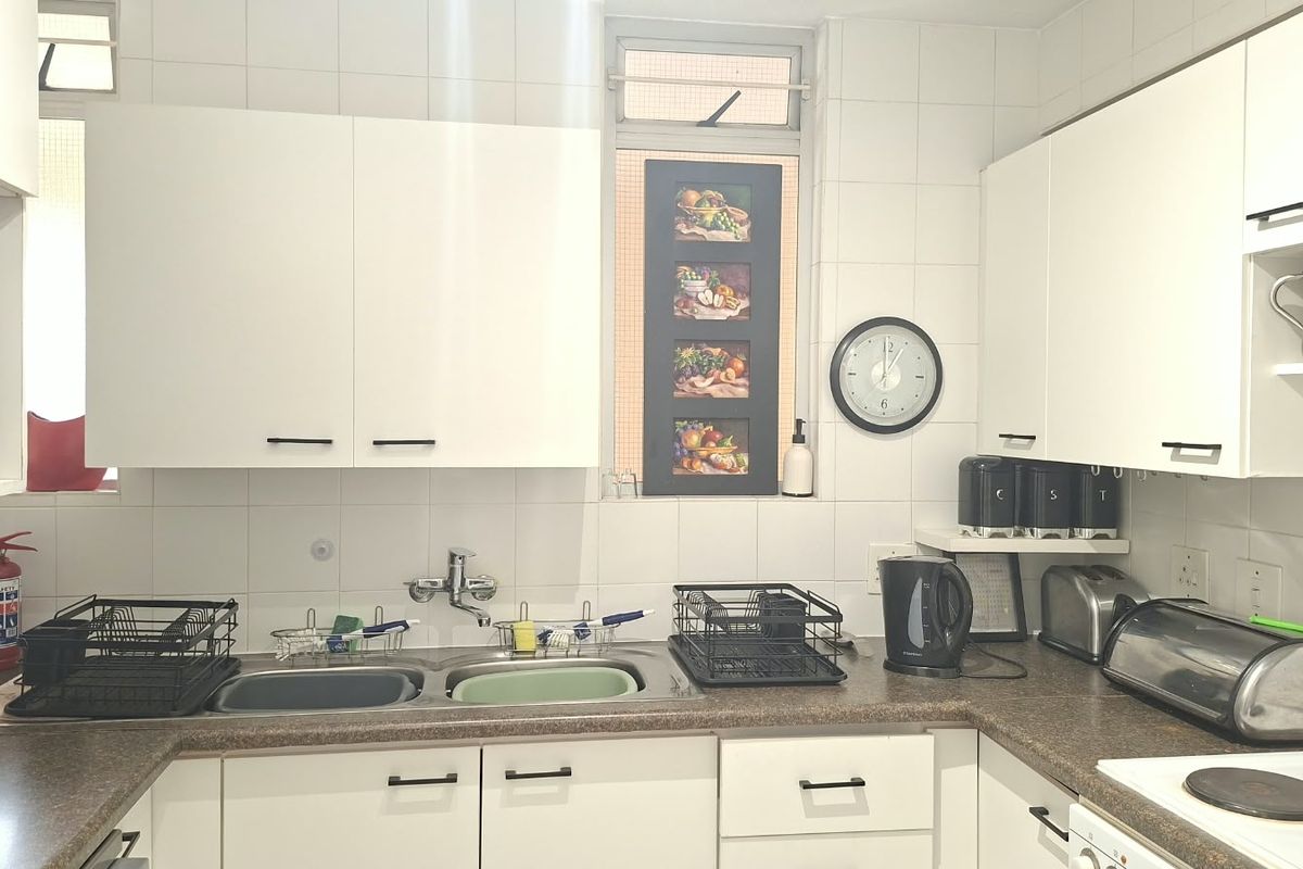 A functional kitchen featuring white cabinetry, a double basin sink, tiled backsplash, and integrated appliances including a microwave and electric hob.