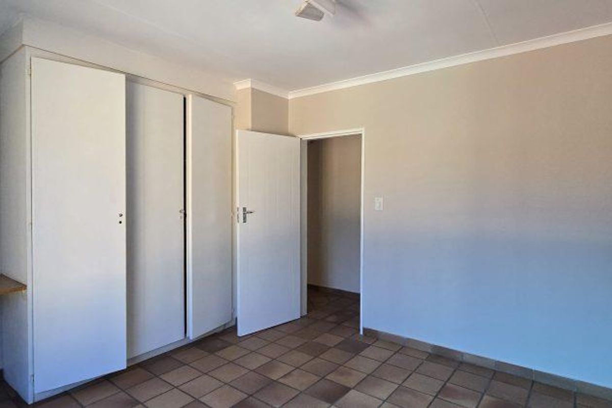 A bedroom featuring built-in cupboards, tiled flooring, and a neutral color palette, offering a clean and functional space.