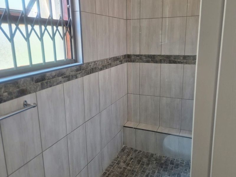 A clean, modern bathroom featuring a walk-in shower with neutral wall tiles, decorative mosaic accents, and a secure window.