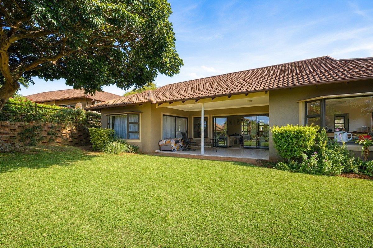 Rear view of the property featuring a covered patio, tiled roof, and a well-maintained garden with a retaining wall.