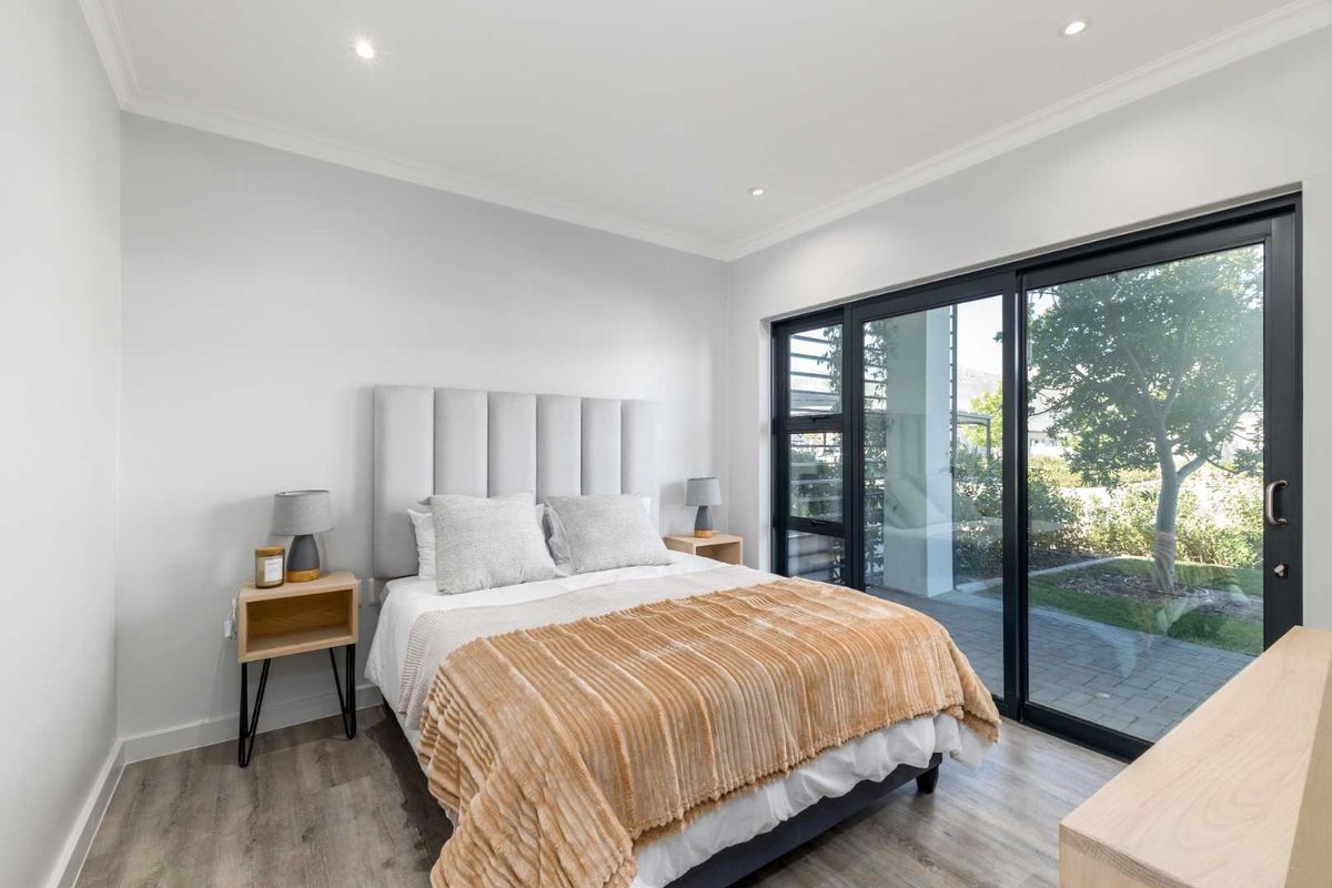 A bright and modern bedroom featuring laminate flooring, recessed downlights, and large sliding glass doors providing direct access to the outdoor area.