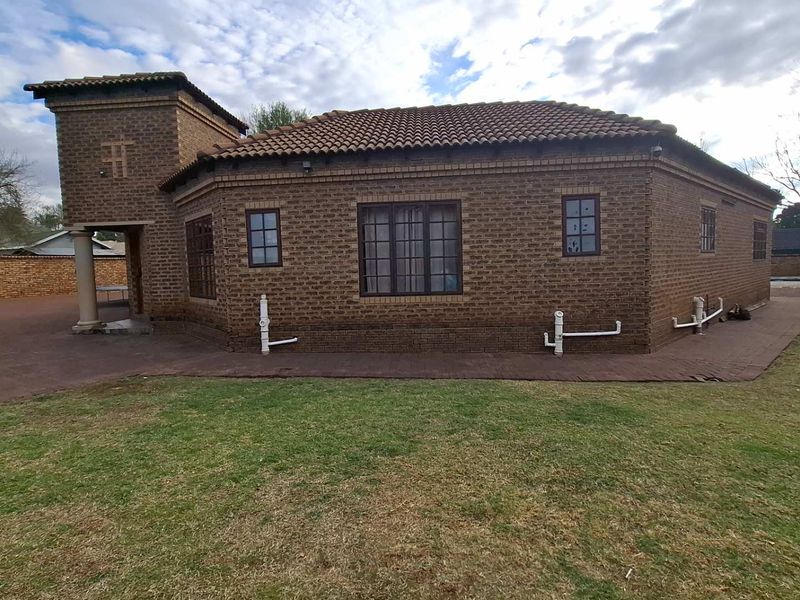 Rear view of a face-brick house featuring a tiled roof, paved perimeter walkway, and established lawn area.