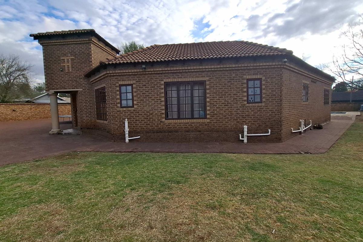 Rear view of a face-brick house featuring a tiled roof, paved perimeter walkway, and established lawn area.