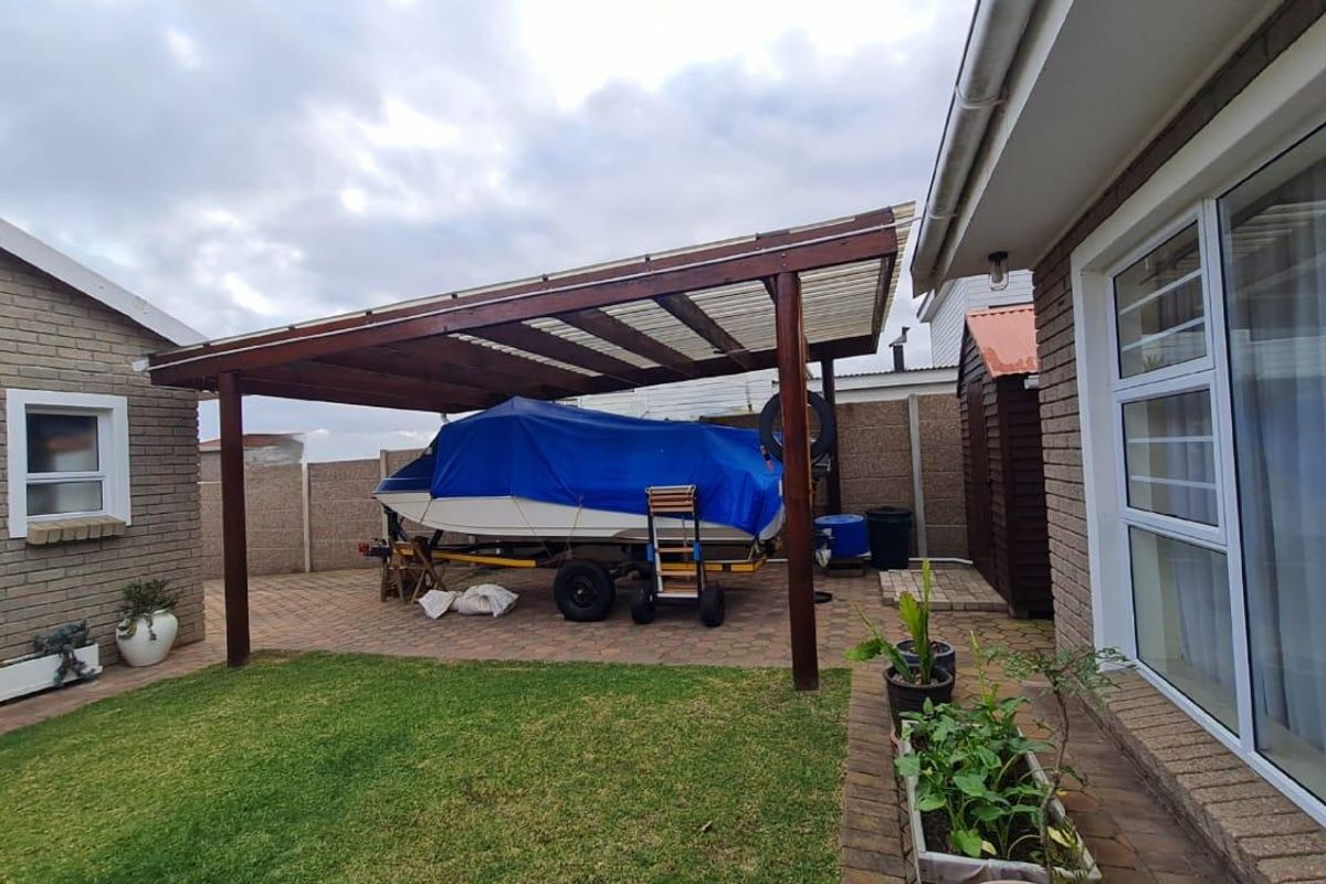 A rear garden area featuring a paved patio with a covered timber pergola structure, brick boundary walls, and a small lawn section.