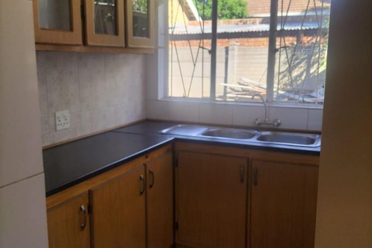 A functional kitchen featuring wooden cabinetry, a double bowl stainless steel sink, and tiled flooring, offering a clean space ready for modernization.