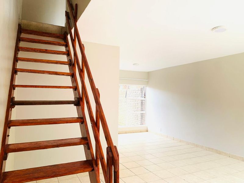 An open-plan living area featuring tiled flooring, recessed lighting, and a prominent wooden staircase leading to the upper level.