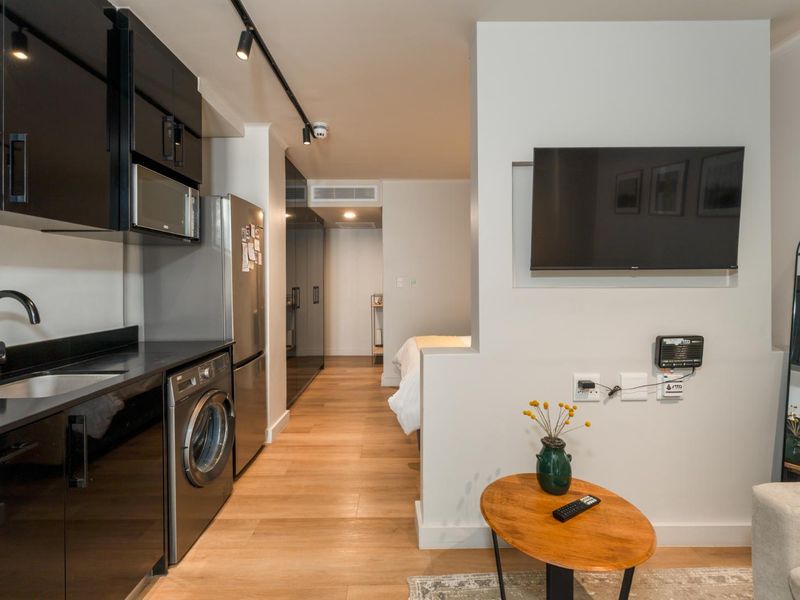 Modern open-plan apartment featuring a sleek black kitchen with integrated appliances, wood flooring, and a dedicated wall-mounted television area.