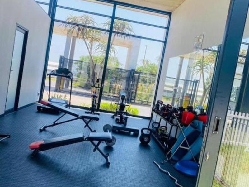 Modern gym facility featuring floor-to-ceiling glass windows, exposed concrete ceilings, and durable rubberized flooring with direct access to the outdoor area.