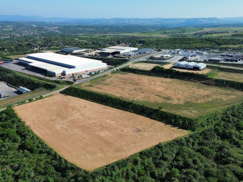 Aerial view of an industrial park featuring large warehouse facilities, paved access roads, and expansive undeveloped land plots surrounded by natural vegetation.