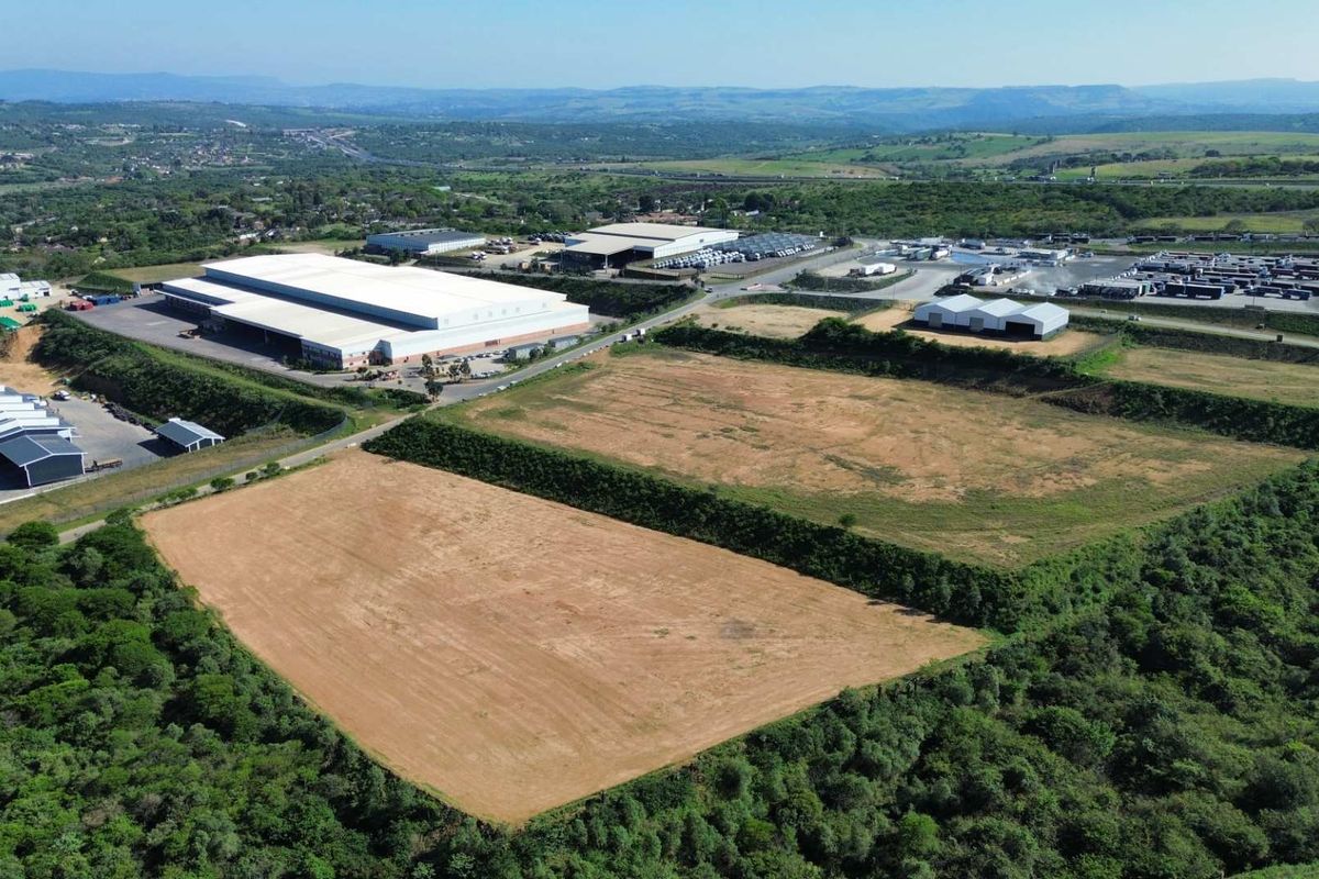 Aerial view of an industrial park featuring large warehouse facilities, paved access roads, and expansive undeveloped land plots surrounded by natural vegetation.