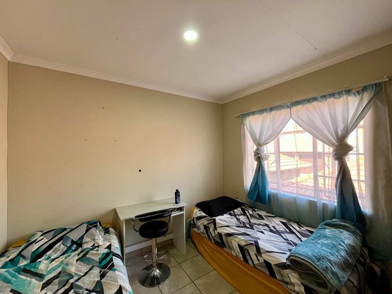 A functional bedroom featuring tiled flooring, a recessed downlight, and a window fitted with security bars.