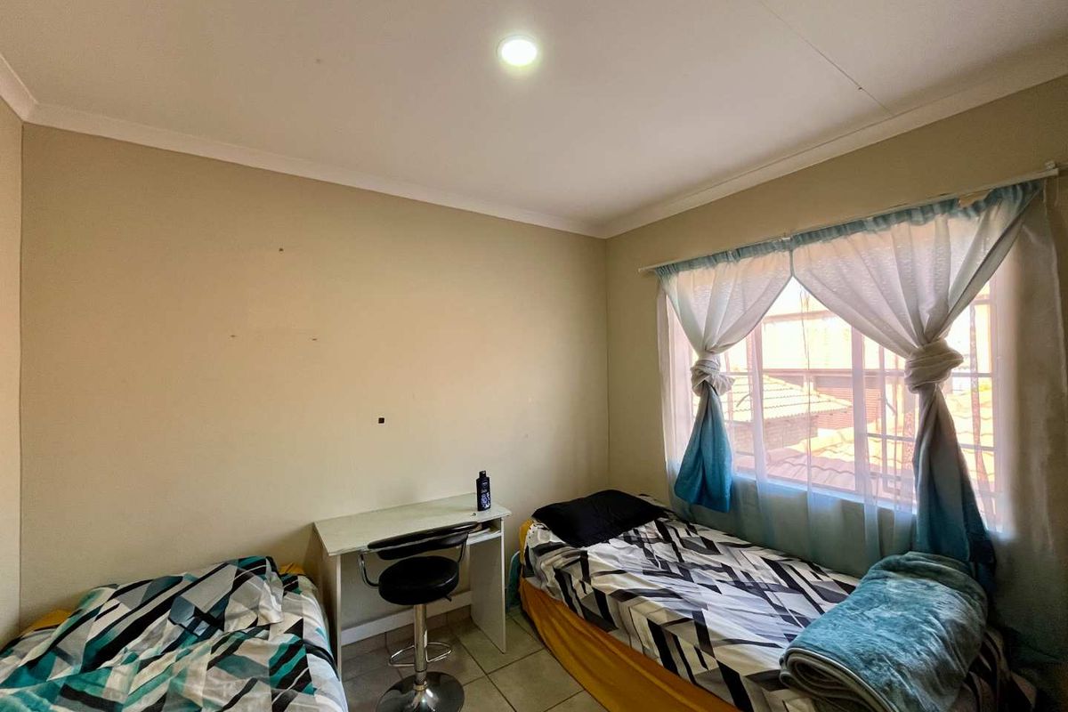 A functional bedroom featuring tiled flooring, a recessed downlight, and a window fitted with security bars.
