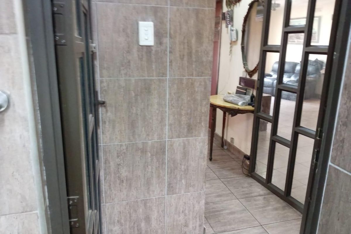 A tiled hallway featuring modern wall tiling and a glass-panelled door leading into the living area.