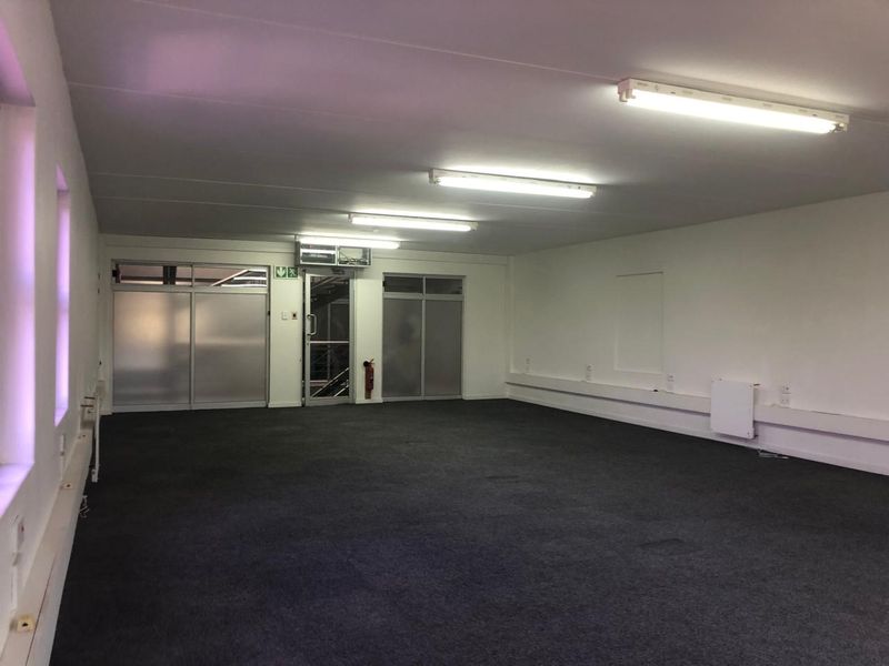 A spacious, empty office area featuring neutral walls, carpeted flooring, and functional fluorescent lighting, suitable for a flexible workspace layout.