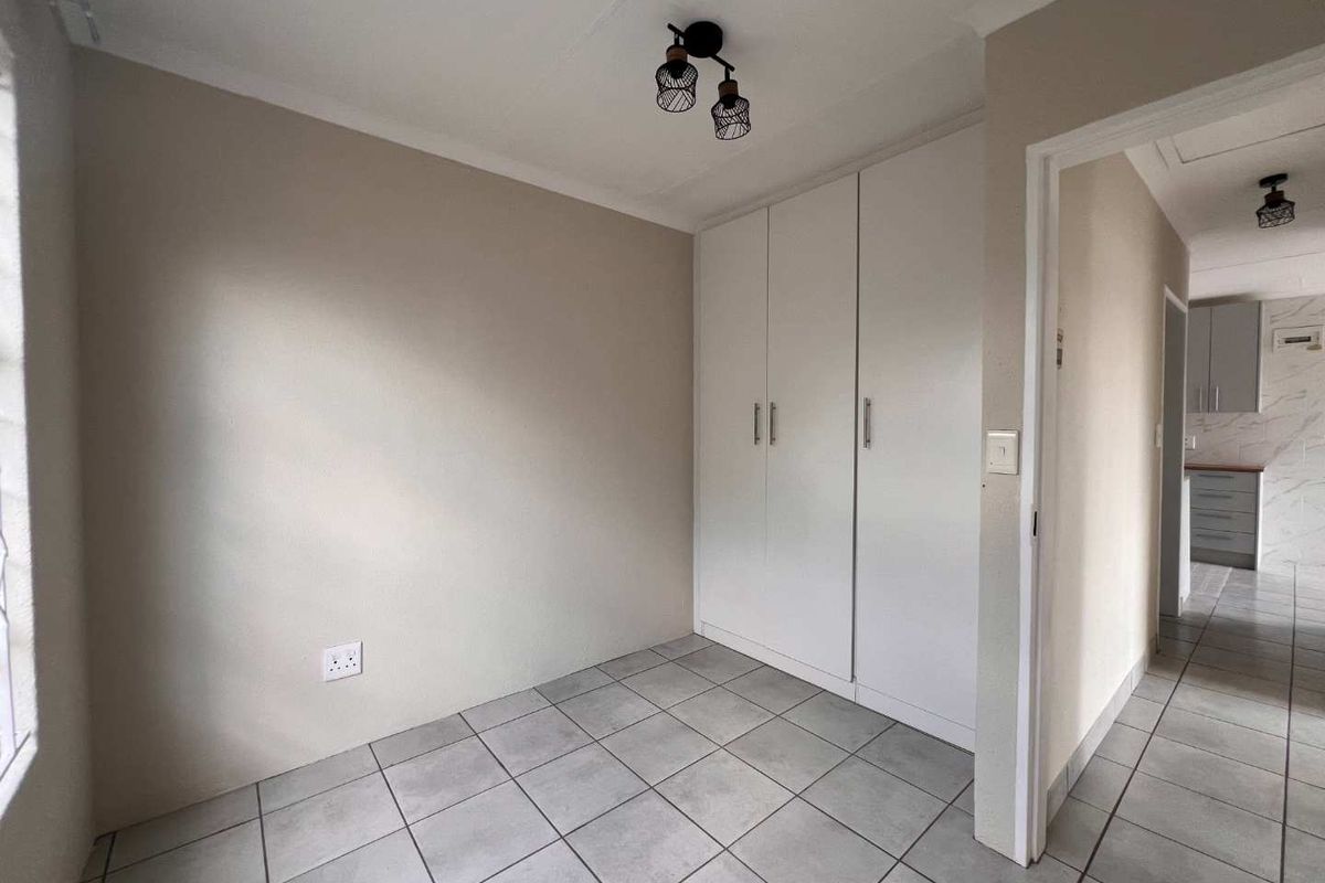 A clean, empty bedroom featuring neutral tiled flooring, built-in white cupboards, and modern ceiling lighting, offering a versatile space ready for personalization.