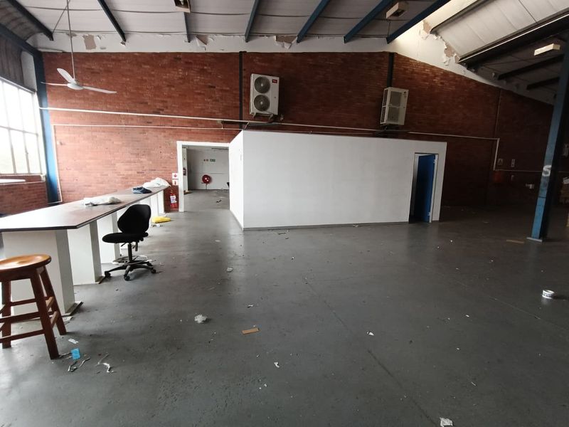 Spacious industrial utility area featuring exposed brick walls, concrete flooring, and high ceilings with exposed steel trusses, suitable for workshop or storage use.