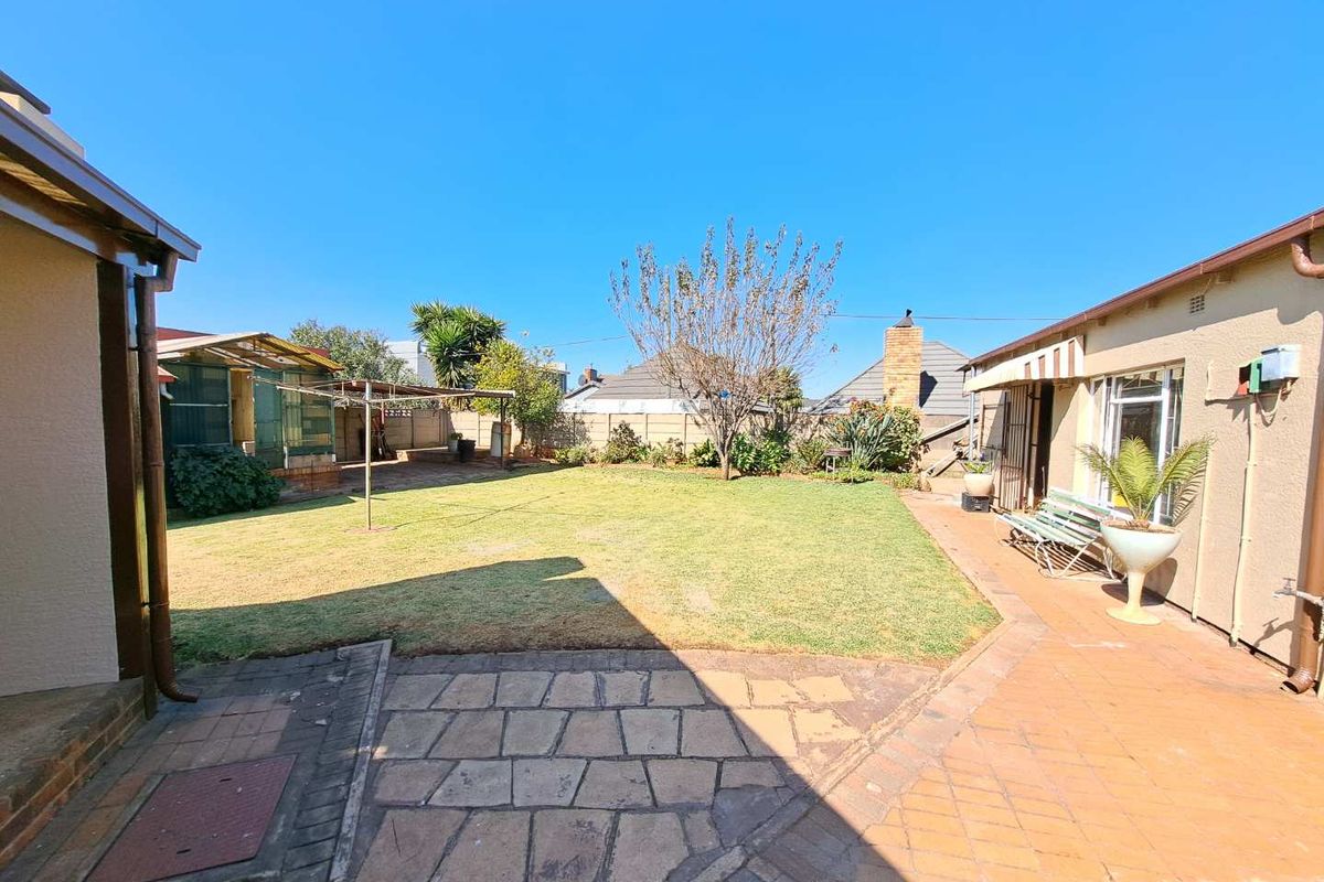 A spacious rear garden featuring a paved patio area, a well-maintained lawn, and perimeter boundary walls.