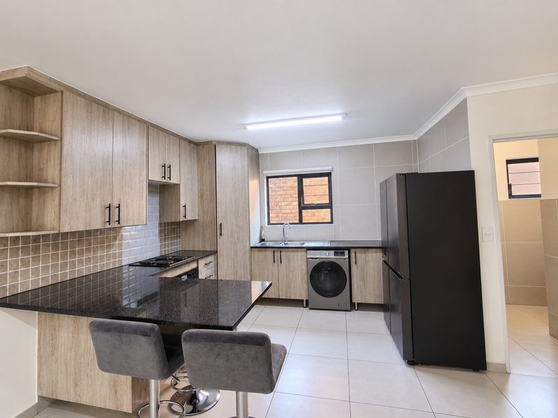 Modern kitchen featuring light wood-grain cabinetry, black granite countertops, tiled backsplash, and integrated appliances, offering a clean and functional workspace.