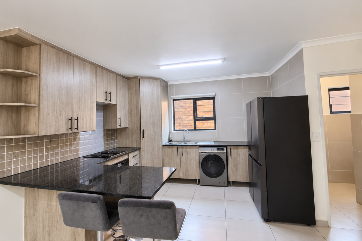 Modern kitchen featuring light wood-grain cabinetry, black granite countertops, tiled backsplash, and integrated appliances, offering a clean and functional workspace.