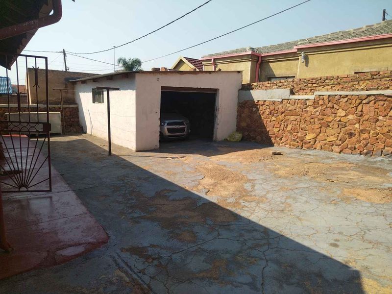 Rear exterior area featuring a detached garage, stone boundary walling, and a concrete driveway with visible surface wear.