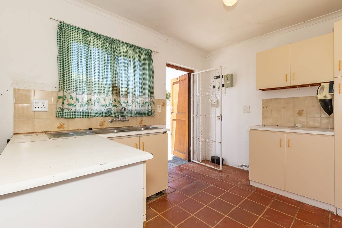 A dated kitchen featuring tiled flooring, laminate cabinetry, a double sink, and direct access to the exterior via a security gate.