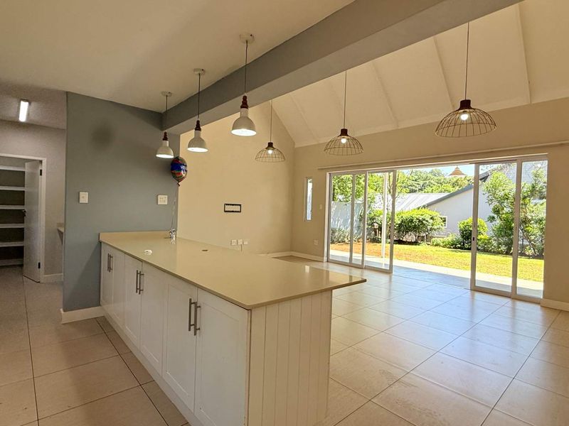 Spacious open-plan kitchen and living area featuring a large island, vaulted ceilings, modern pendant lighting, and seamless access to the rear garden via sliding doors.