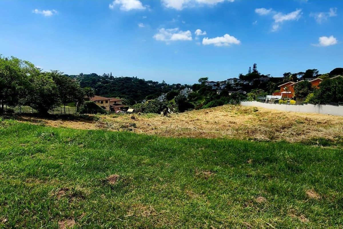 A vacant residential plot featuring established grass, boundary walling, and scenic views of the surrounding neighborhood.