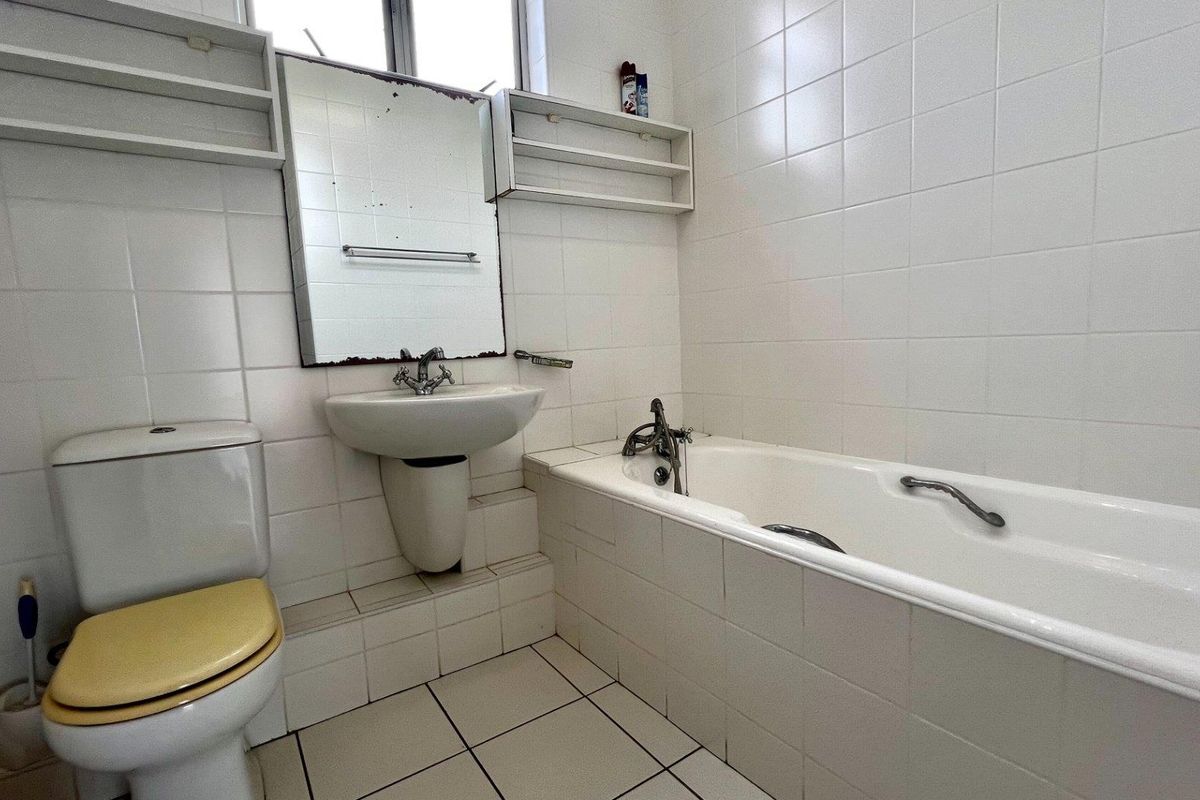 A functional bathroom featuring a pedestal basin, bathtub, and tiled finishes, currently requiring cosmetic updates to modernize the space.