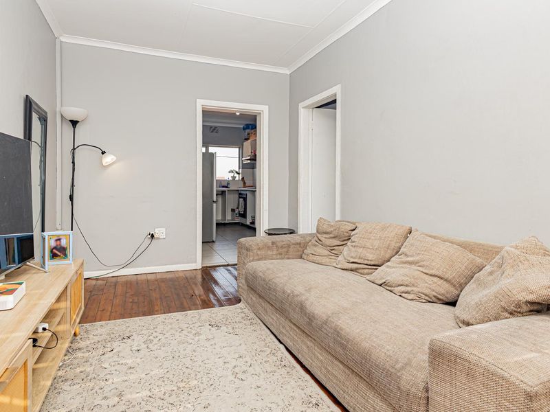 A living room featuring hardwood flooring and coved ceilings, with a doorway leading to the kitchen area.