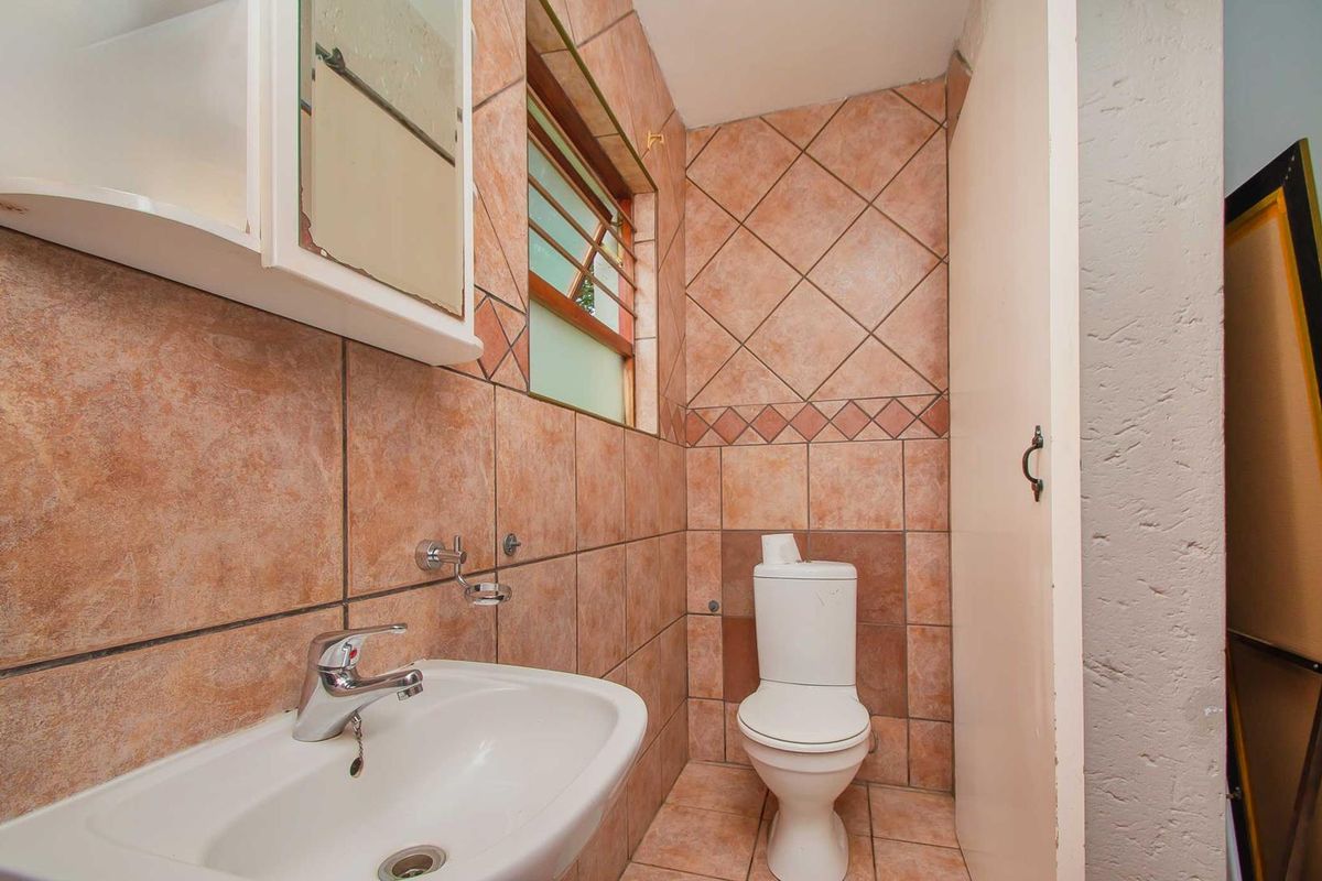 A compact bathroom featuring ceramic wall and floor tiles, a pedestal basin, and a standard toilet.