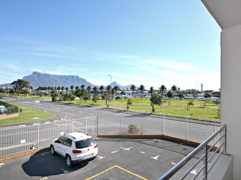 Elevated view from a balcony overlooking a parking area, surrounding landscape, and distant mountain scenery.