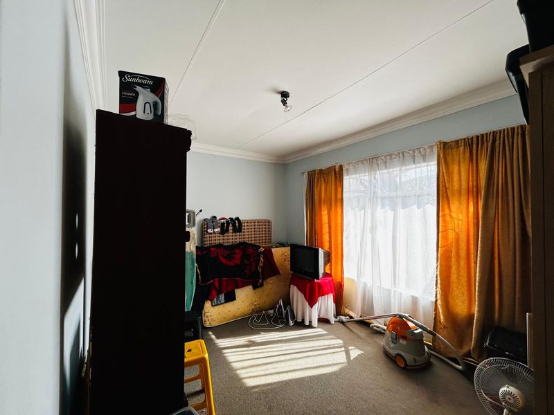 A bedroom featuring carpet flooring and decorative ceiling cornicing, illuminated by natural light through a large window.