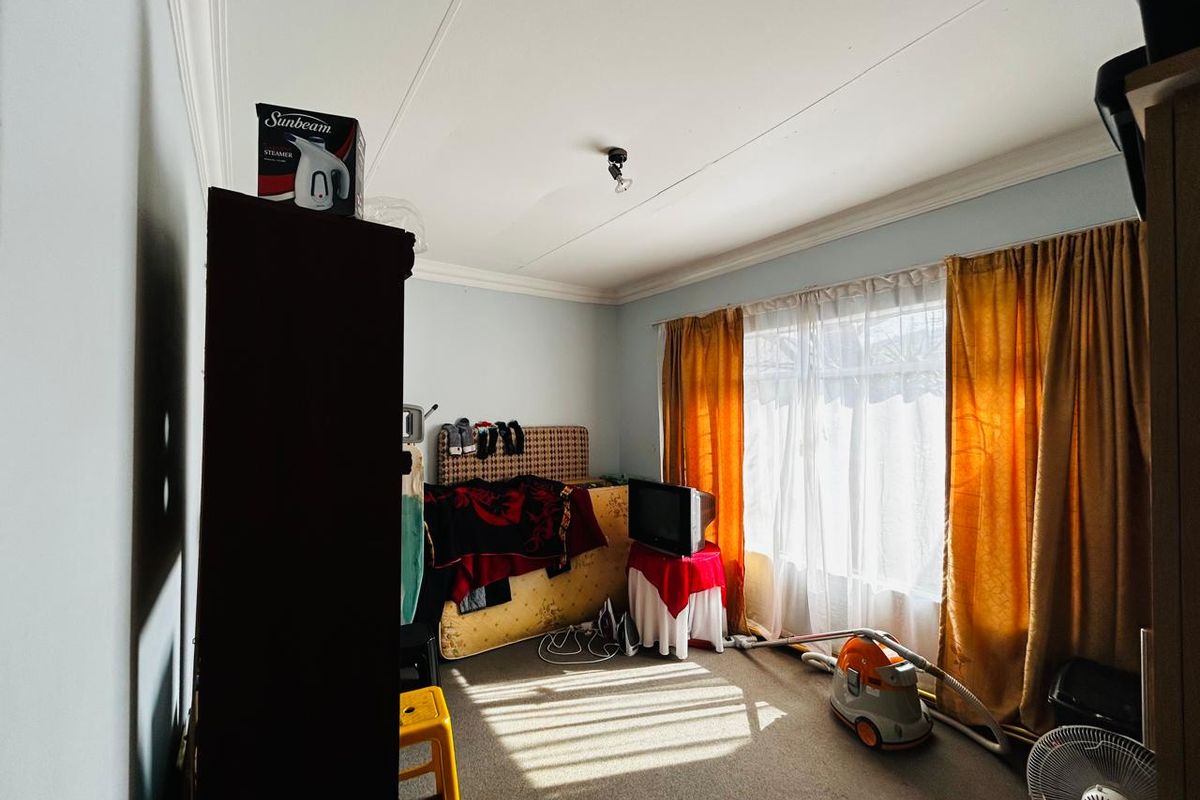 A bedroom featuring carpet flooring and decorative ceiling cornicing, illuminated by natural light through a large window.