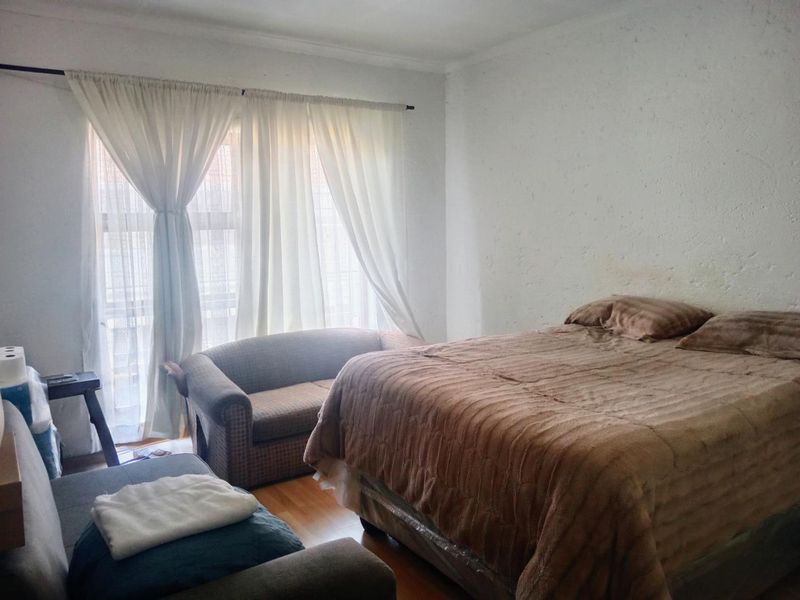 A bedroom featuring laminate flooring and large windows with curtains. The walls show visible signs of wear and staining.