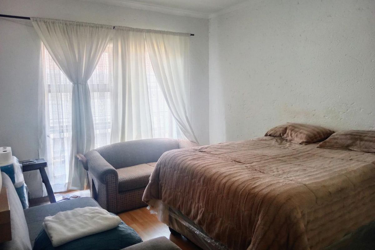 A bedroom featuring laminate flooring and large windows with curtains. The walls show visible signs of wear and staining.
