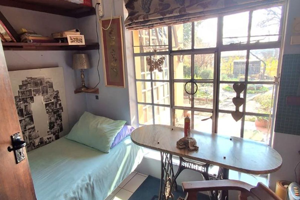 A compact bedroom featuring tiled flooring, built-in shelving, and a large steel-framed window providing natural light and garden views.