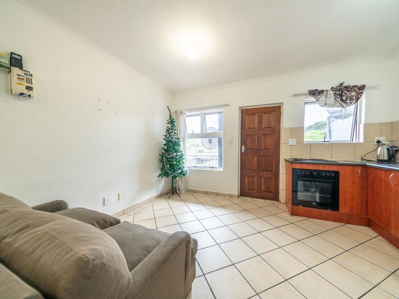 Open plan living area featuring tiled flooring, a compact kitchen with built-in oven and hob, and direct access to an exterior door.