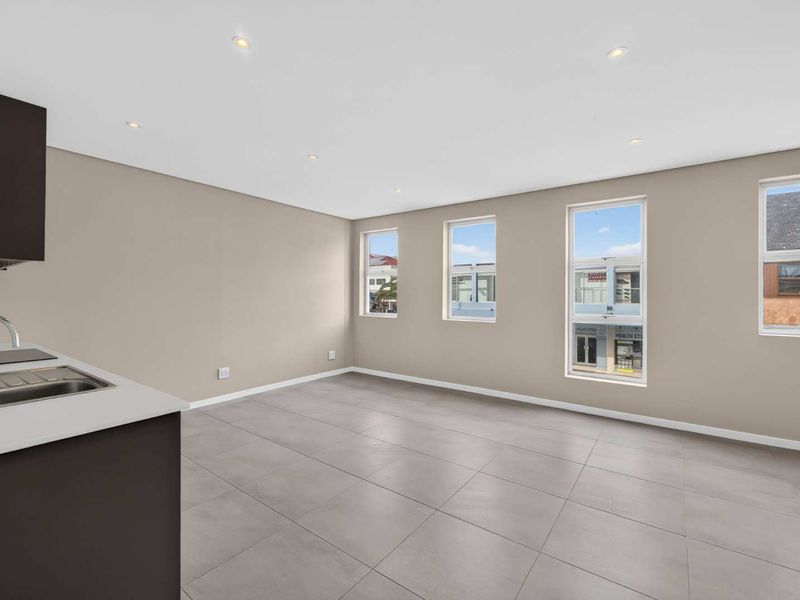 A bright, modern open-plan living and kitchen area featuring neutral walls, large windows, recessed lighting, and contemporary tiled flooring.