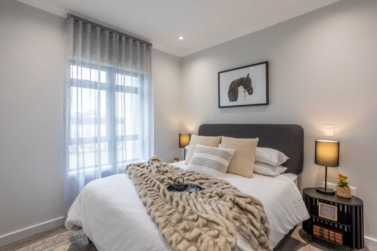 A well-lit, modern bedroom featuring neutral wall tones, recessed ceiling lighting, and a large window with elegant sheer curtains.