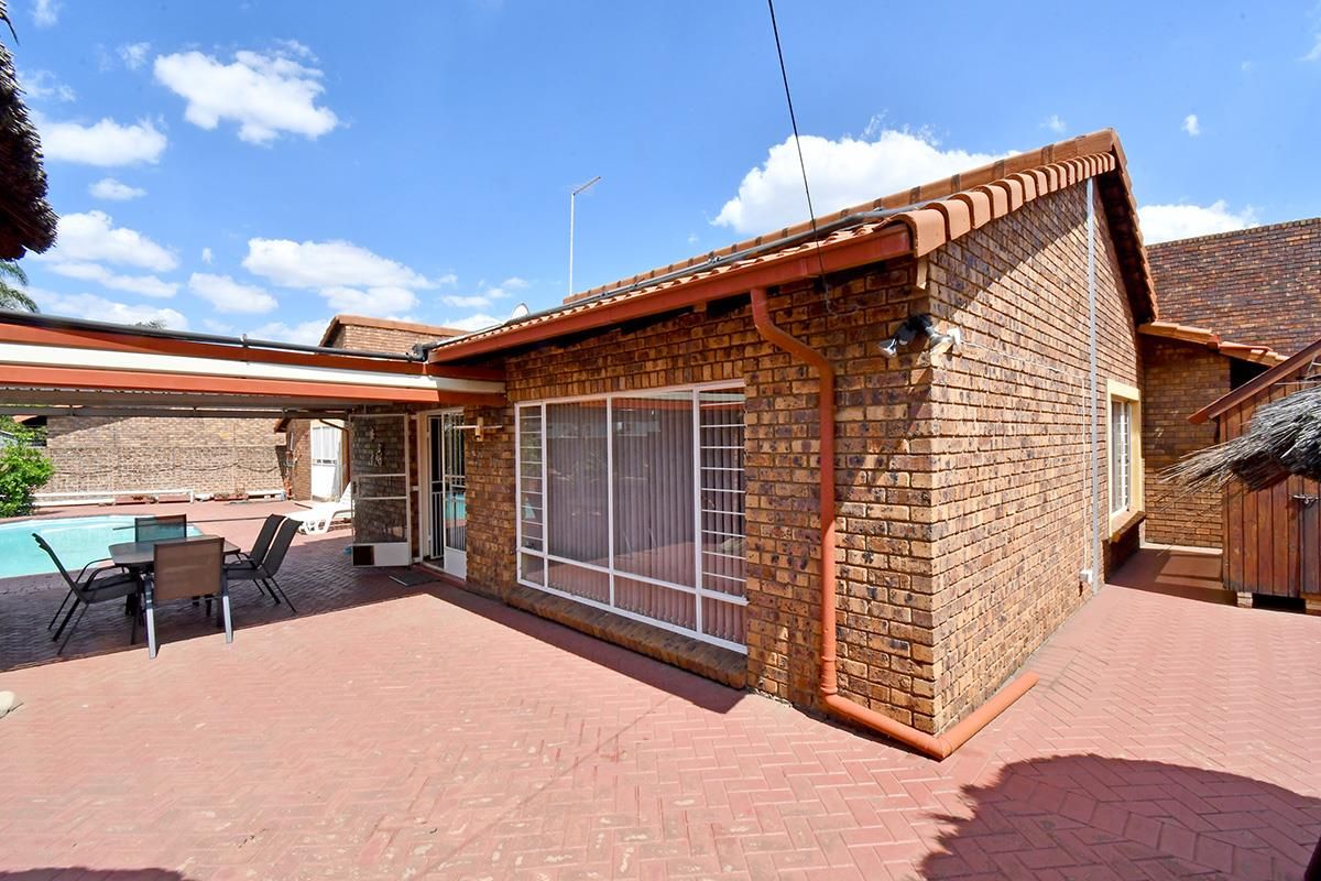 Rear exterior view featuring a paved patio area, brick facade, and access to the swimming pool.