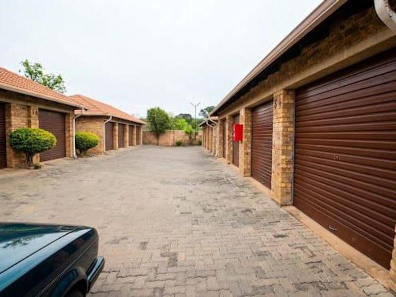 A row of brick-built garages with brown roller shutter doors and a paved driveway in a residential townhouse complex.