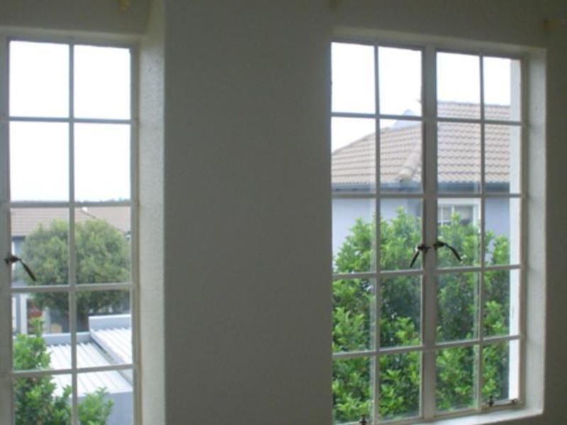 An empty bedroom interior featuring two large casement windows with views of the surrounding residential area.