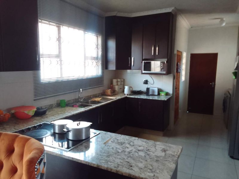A functional kitchen featuring dark wood cabinetry, granite countertops, a built-in hob, and a built-in microwave, with tiled flooring throughout.