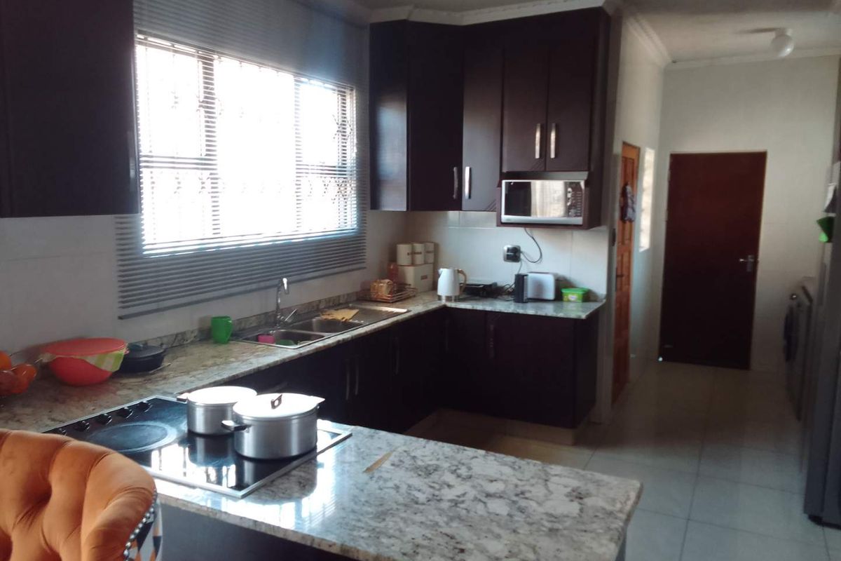 A functional kitchen featuring dark wood cabinetry, granite countertops, a built-in hob, and a built-in microwave, with tiled flooring throughout.