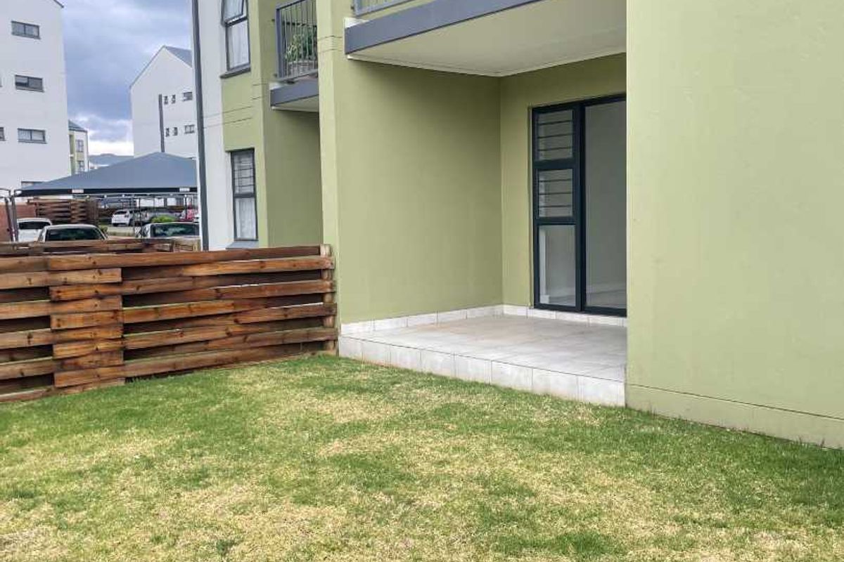 Ground floor apartment exterior featuring a private tiled patio, small lawn area, and wooden boundary fencing.