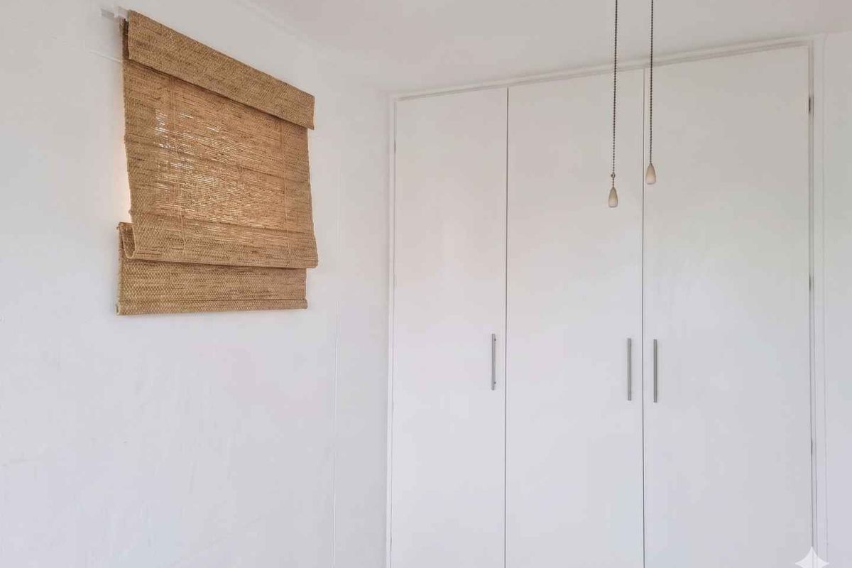 A bright bedroom featuring built-in white cabinetry with modern handles and a ceiling fan, providing clean and functional storage space.